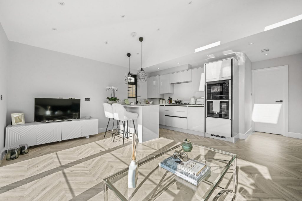 Modern open-plan kitchen at 86 Holmesdale Road, with breakfast bar, pendant lights, and integrated appliances, featuring herringbone flooring and a minimalist living area.